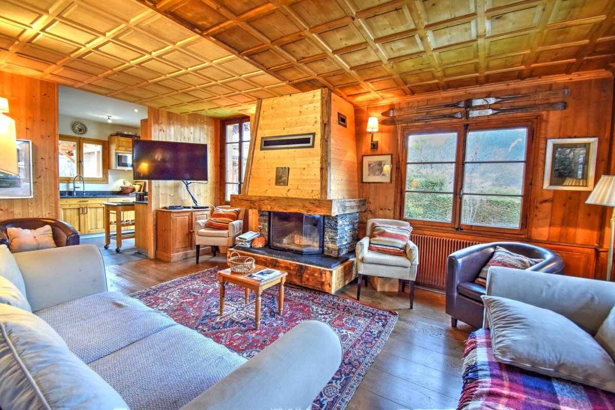Cozy alpine chalet living room featuring wood-paneled walls, a coffered ceiling, a stone fireplace, and comfortable seating.