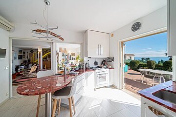 Bright kitchen with red terrazzo countertops and an open sliding door leading to a sunny deck with an ocean view.