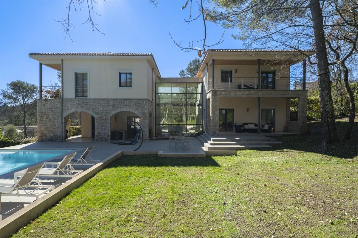 Modern two-story house with a glass link, pool, and green lawn on a sunny day.