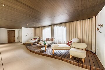Modern spa relaxation area with elegant lounge chairs on a curved wooden deck under a warm wood-paneled ceiling.