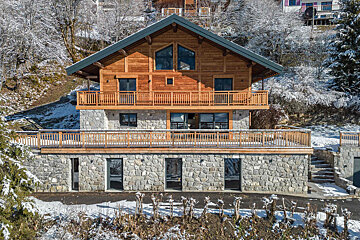 A large house with a wooden roof is surrounded by snow