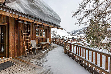 A snowy deck with a table and chairs on it