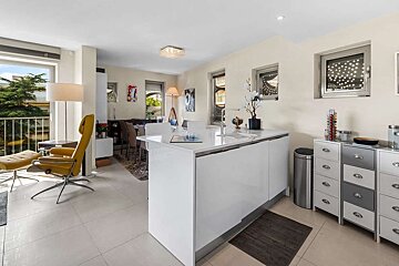 Bright, modern open-plan kitchen and living space featuring a white island, yellow lounge chair, and balcony access.
