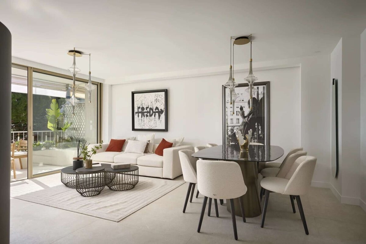 A modern, bright open-plan living and dining room with a white sofa, elegant dining set, large artworks, and a sunny balcony view.