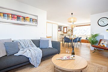 Modern, open-plan living and dining room with a grey sofa, wooden coffee table, and cozy, bright decor.