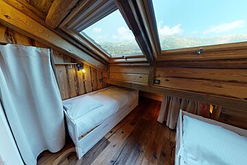 Cozy, wood-paneled attic bedroom with two single beds and a large skylight offering a panoramic view of mountains and sky.