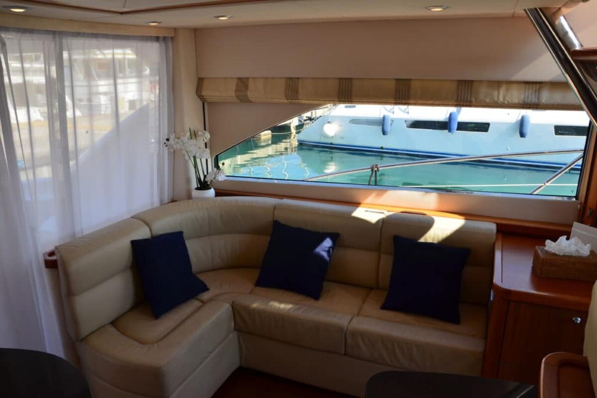 A couch with blue pillows sits in front of a window with a boat in the background