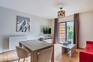 A modern living/dining space with wood floors, a dining table, red sofa, mountain painting, and a unique cow-print light fixture.
