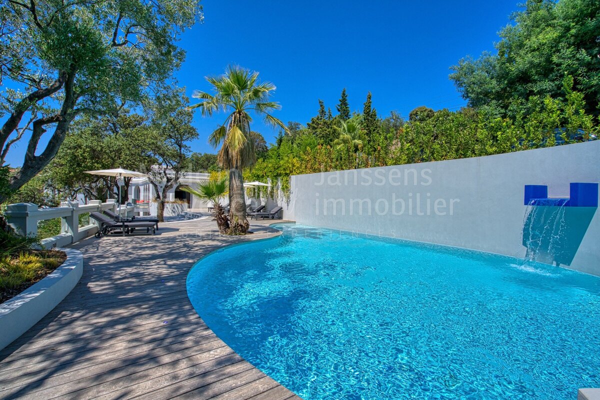A large swimming pool is surrounded by a white wall that says janssens immobilier