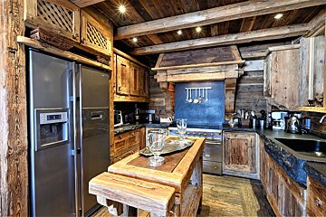 A rustic, luxurious chalet-style kitchen. It features abundant dark wood, exposed beams, modern stainless steel appliances, and a central wooden island.