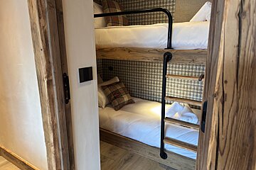 Rustic wooden bunk beds with plaid accents and a black metal ladder, viewed through an open doorway.