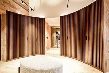 Modern room with curved, vertical-slatted wooden wardrobes, a light wood floor, and a round textured ottoman.