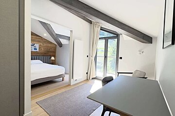 Bright, modern apartment interior with an open-plan bedroom and living area, featuring an angled ceiling and balcony view.