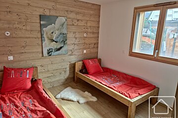 Cozy room with two wooden single beds, red ski-themed bedding, a polar bear picture on a wooden wall, and a window with an outdoor view.