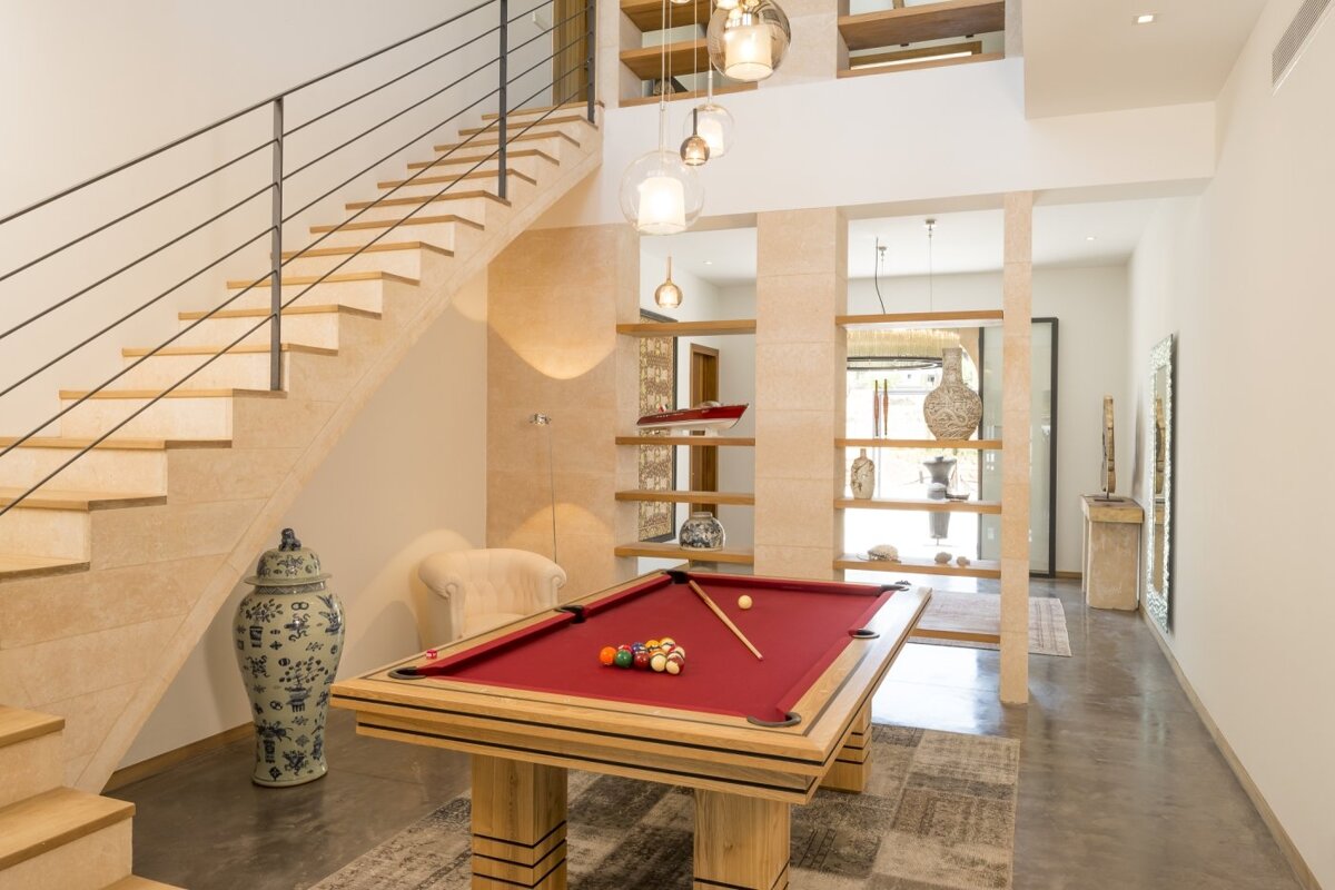 A pool table in a hallway under a staircase