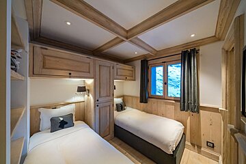 Rustic, cozy bedroom with two single beds, warm wooden paneling, built-in cabinets, and a window offering a bright view.