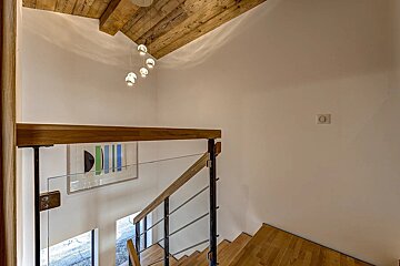 Modern interior with a wooden beamed ceiling, contemporary chandelier, and a stylish staircase with wood steps, metal, and glass railings leading down.
