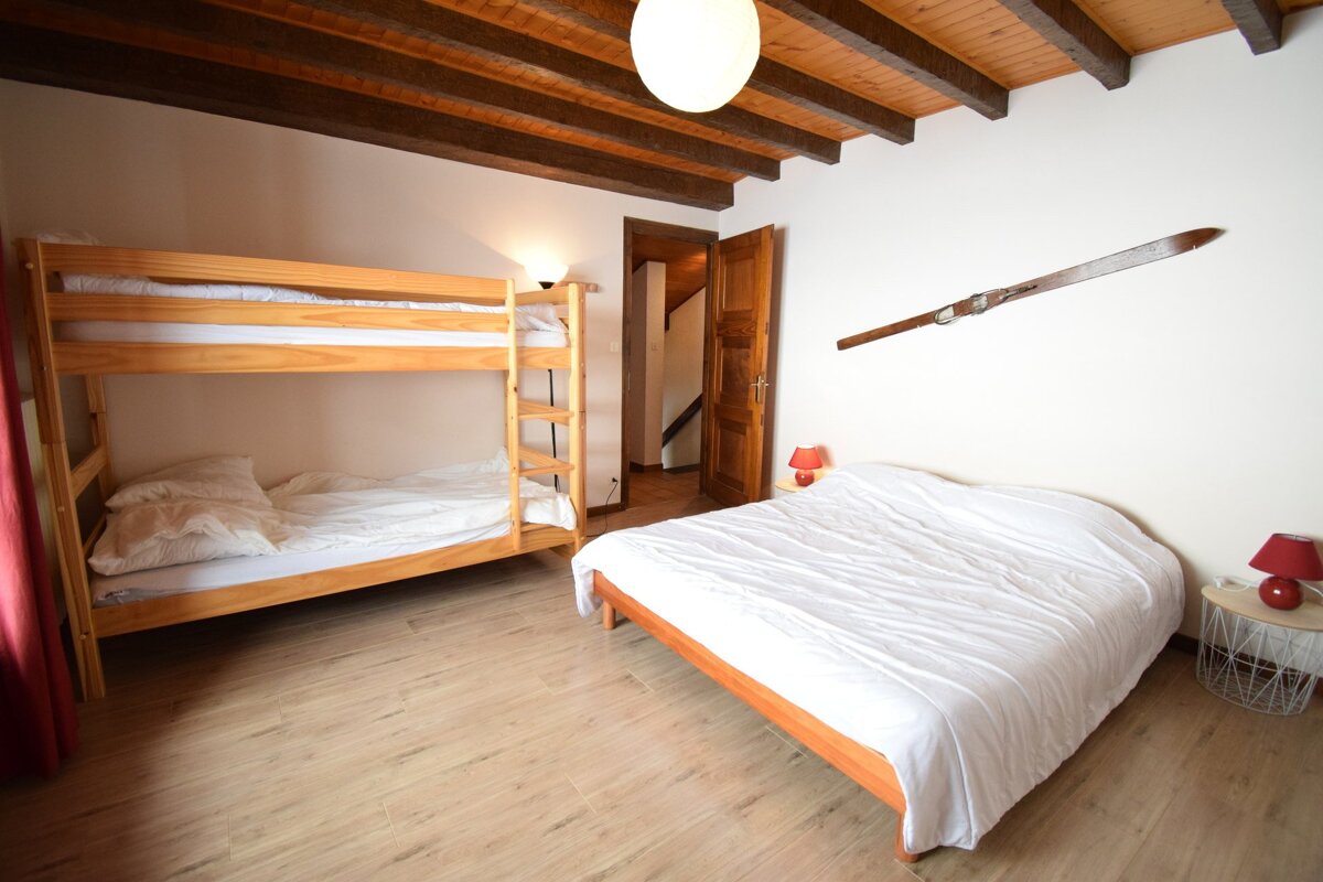 Rustic bedroom with a wooden bunk bed, a double bed, exposed ceiling beams, and a decorative wooden ski on the wall.
