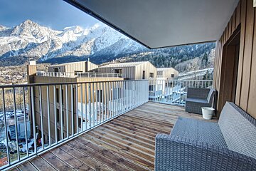 A balcony with mountains in the background and a couch and chair