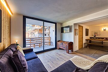 Cozy living room featuring purple sofas, a rustic wooden chest, and sliding glass doors opening to a balcony with alpine views.