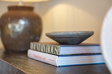 Two stacked books with a small bowl on top sit on a wooden surface next to a ceramic lamp, captured in a warm, soft-focus shot.