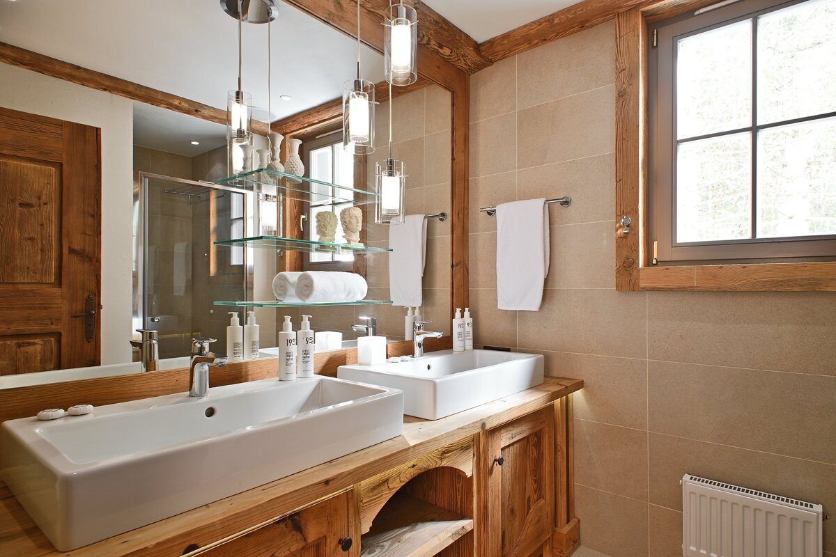 Spacious, rustic-modern bathroom with dual vessel sinks on a wooden vanity, a large mirror with hanging lights, and a window.