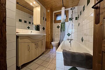 A cozy bathroom features white tiled walls with green diamond accents, a wooden ceiling, a sink vanity, toilet, and a bathtub with a shower and patterned curtain.