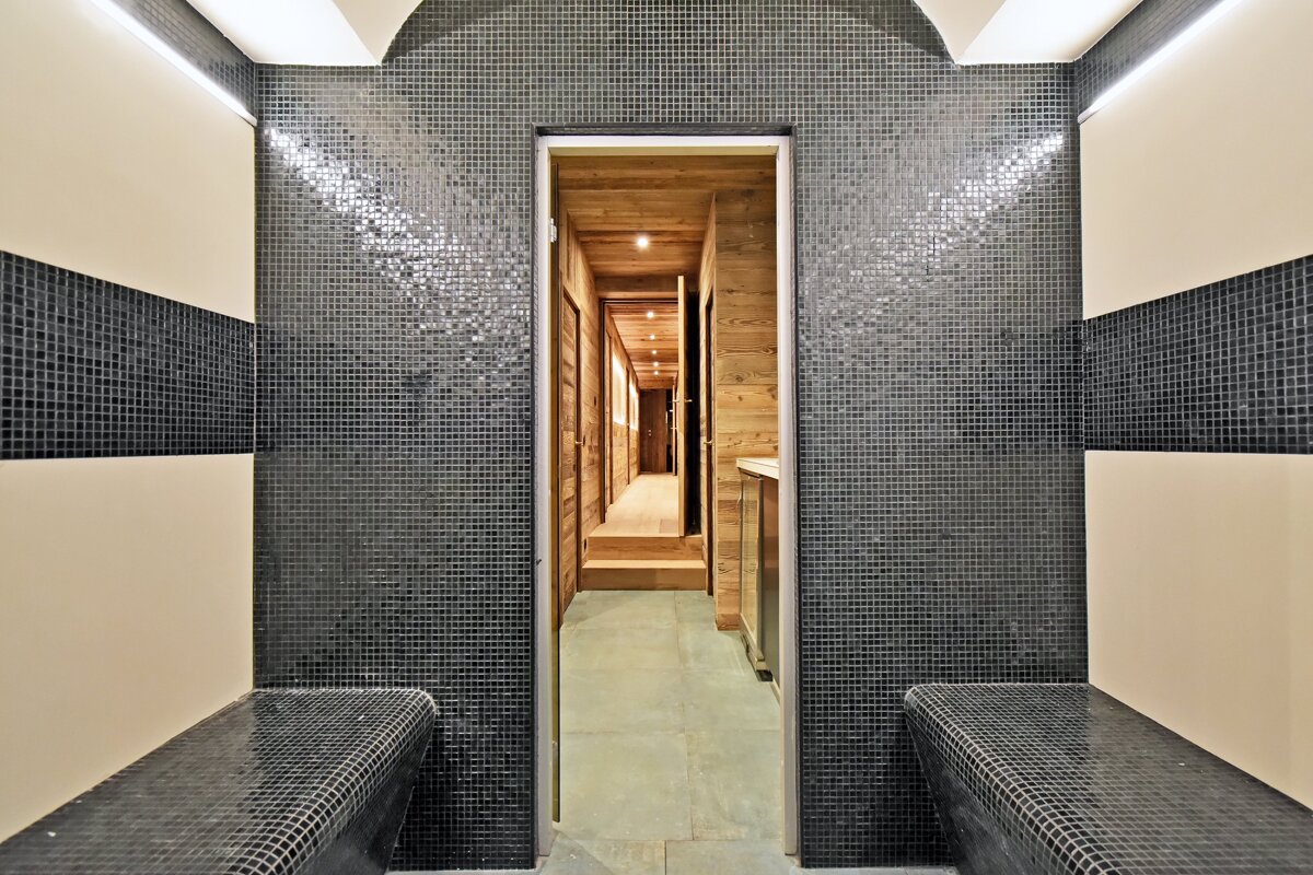 A bathroom with black tiles and a wooden hallway