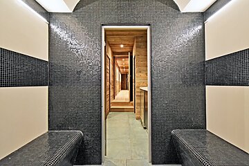 A bathroom with black tiles and a wooden hallway