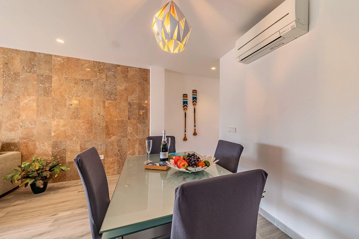 A dining room table with a bowl of fruit and a bottle of wine