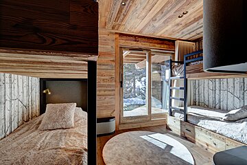 Cozy, wood-paneled bunk bedroom with birch tree wallpaper and plush bedding, featuring a sliding door to a snowy outdoor scene.