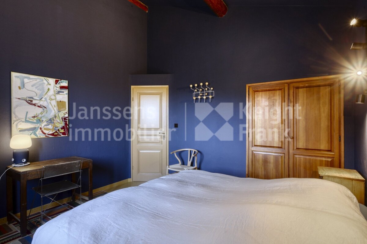 A bedroom with a bed and a painting on the wall and the words janssen immobilier on the wall
