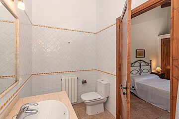 A bathroom with a toilet and a sink leading to a bedroom