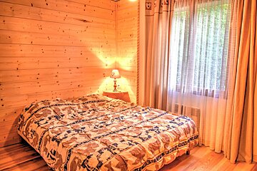 A cozy wood-paneled bedroom with a patterned bed, bedside lamp, and a window with curtains letting in natural light.