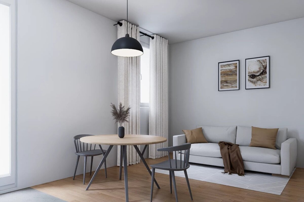 Minimalist living area featuring a round wooden table with grey chairs, a black pendant light, and a white sofa with brown cushions.