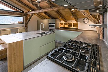 Modern kitchen with green cabinets, concrete counters, a gas stove, and a wooden beamed ceiling. A window offers a mountain view.