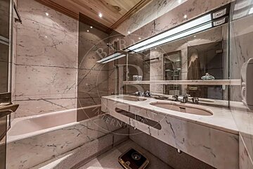 A luxurious bathroom featuring pink marble walls, a bathtub, a double vanity with two sinks and a large mirror, and a warm wooden ceiling.