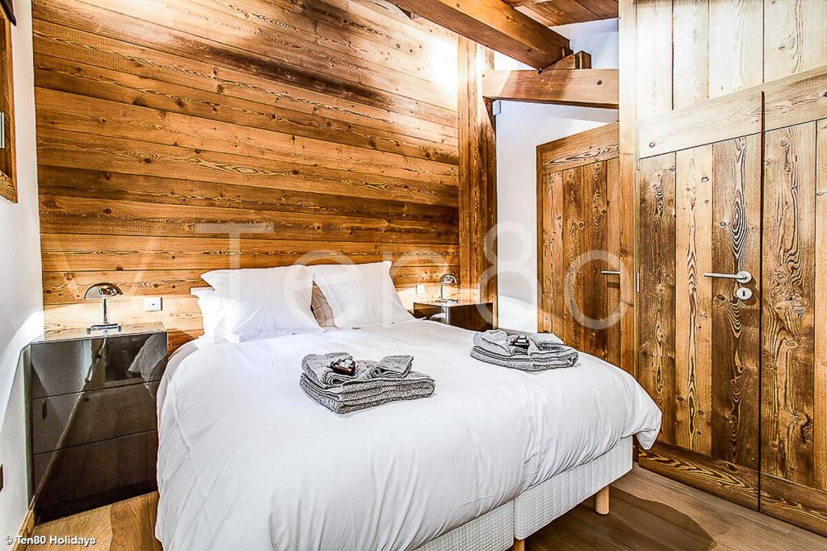 A bedroom with wood paneling and a bed with white sheets