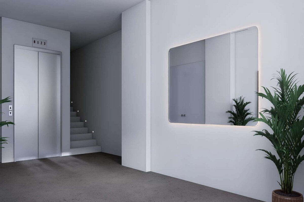 A minimalist hallway features an elevator, illuminated stairs, and a backlit mirror reflecting a plant, alongside a potted palm, in a clean, modern design.