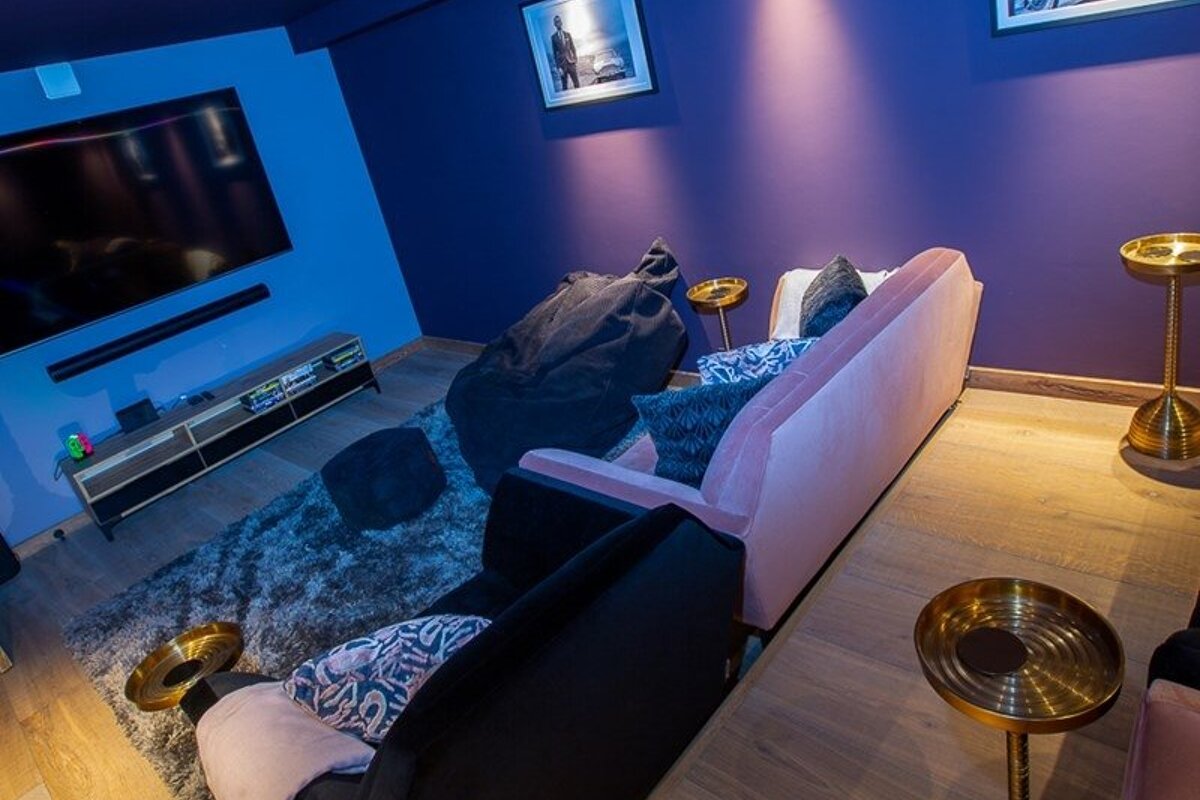 Cozy home media room featuring a pink sofa, black armchair, shag rug, large TV, and colorful blue and purple walls.