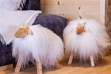 Two decorative wooden sheep with fluffy white wool standing on a wooden floor next to a couch.