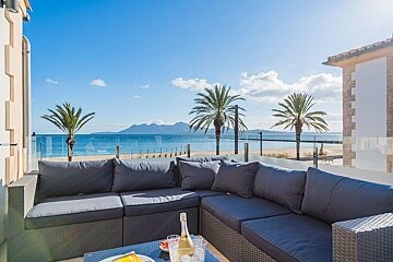 A couch with a bottle of champagne on it sits on a balcony overlooking the ocean