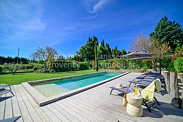 A large swimming pool is surrounded by lawn chairs and umbrellas and is for sale by provence immobilier