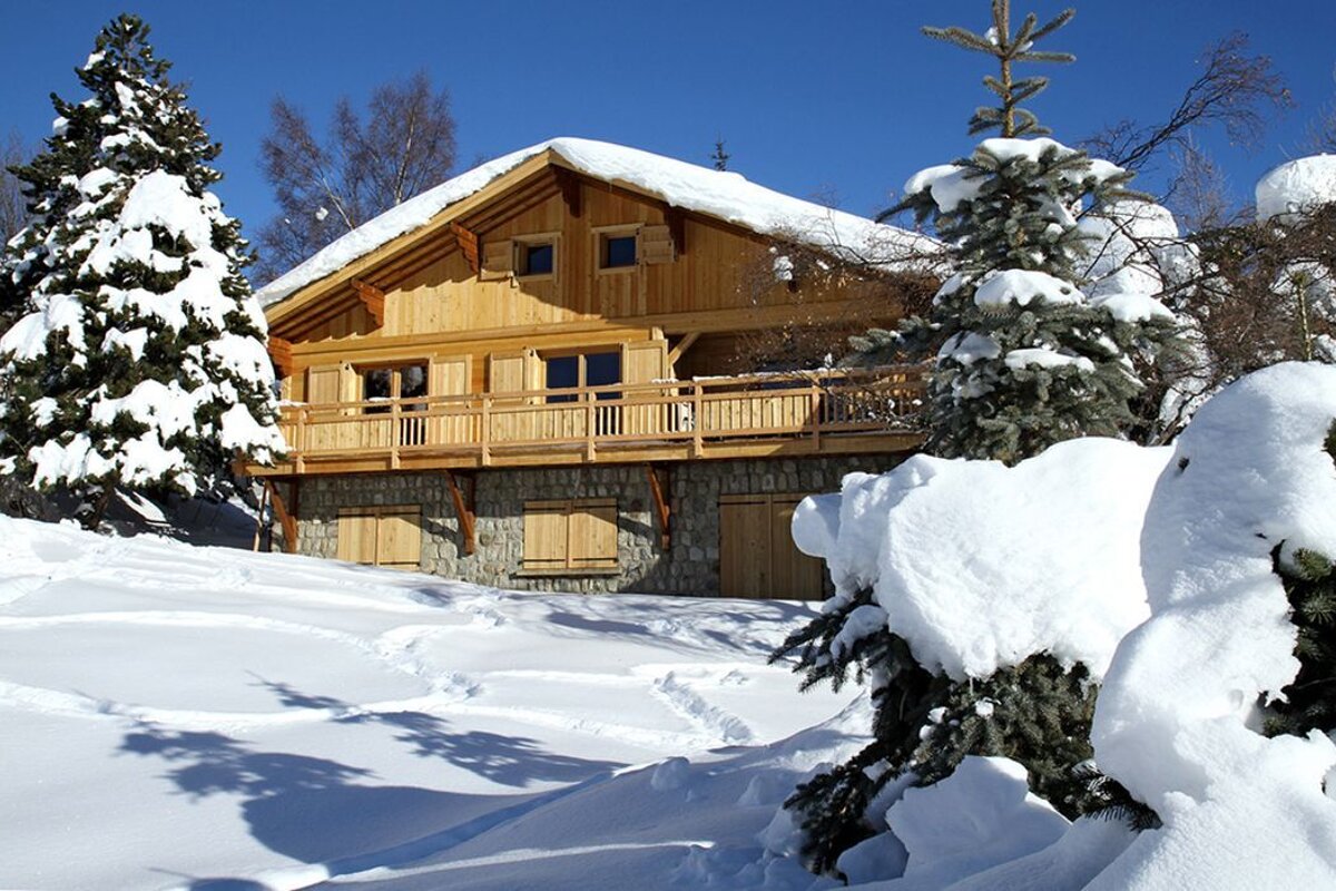 Snow covered trees in front of a wooden house
