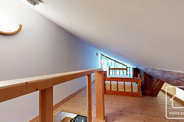 An attic bedroom with sloped ceilings, a wooden bed, light wood floors, and a railing overlooking stairs.