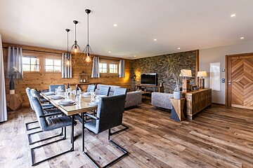 Modern chalet interior featuring a wooden dining area with grey chairs and an open living room with a stone accent wall.