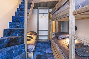 Cozy cabin bedroom featuring blue carpeted stairs, rustic wooden bunk beds, and a small closet.