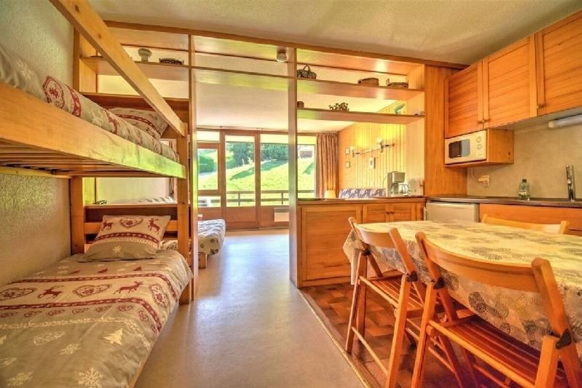 Cozy wooden cabin interior featuring bunk beds, a dining table, and a scenic green hillside view through large glass doors.