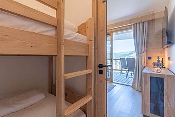 Wooden bunk beds in a bedroom looking into a bright area with a balcony and scenic mountain views.