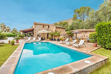 A large swimming pool surrounded by chairs and umbrellas in front of a house